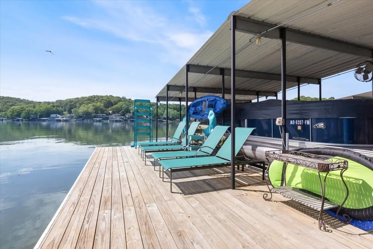 A vibrant dock scene with lounge chairs, two kayaks, and lake views surrounded by trees. The dock is ideal for sunbathing, launching kayaks, fishing, or simply enjoying the water, showcasing the adventure and recreation available steps away from the property.