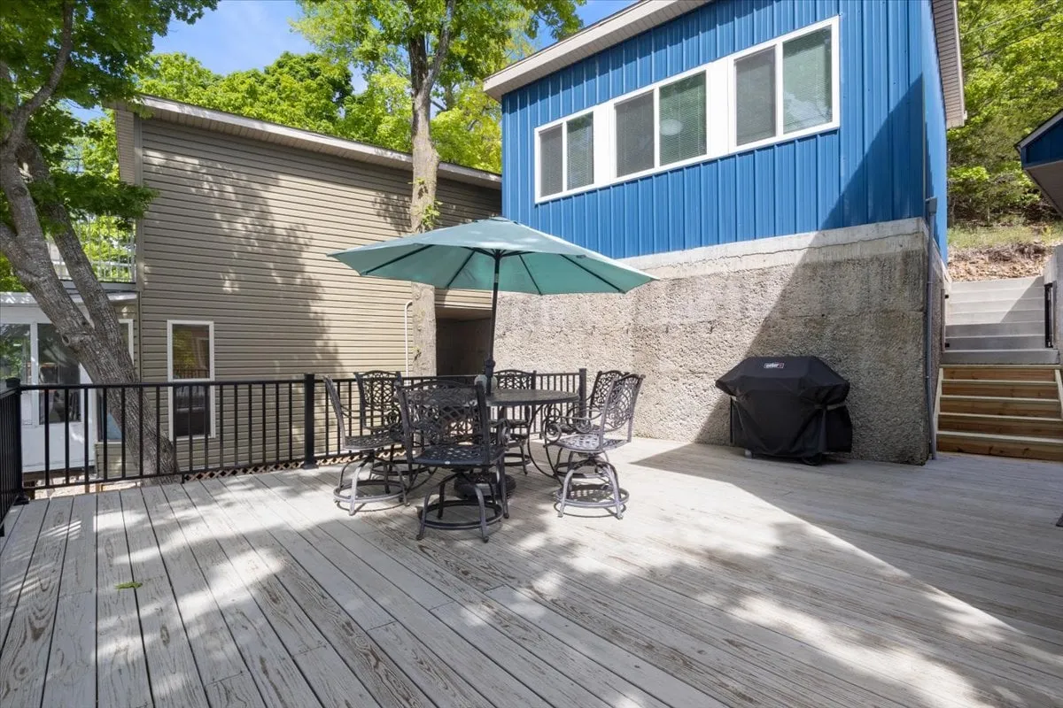 A casual stone patio with an outdoor dining set, green umbrella, and a backdrop of blue house siding. The space is ideal for barbecues or casual evening gatherings under the stars, offering a different angle on the property’s social spaces.