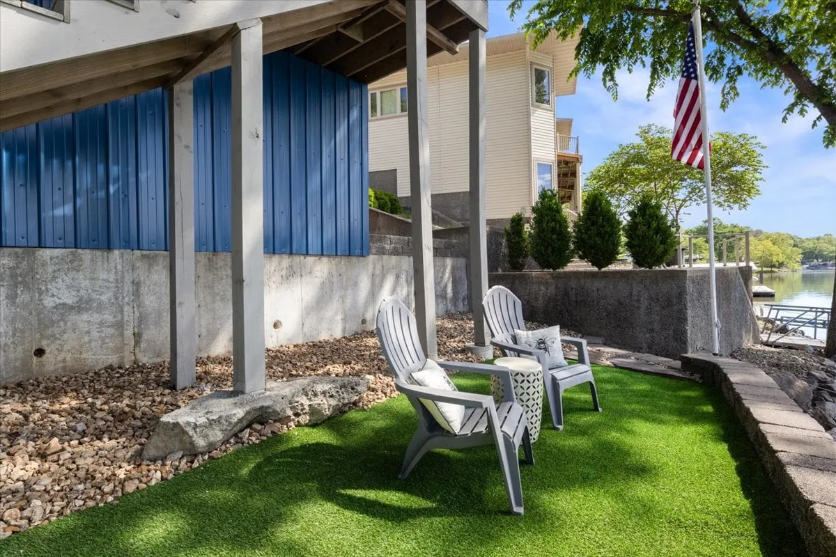 A cozy turf patio area featuring two comfortable chairs on artificial grass, complemented by an American flag and a blue wall in the backdrop. The space is ideal for relaxing, socializing, or enjoying a book, all with a hint of lakeside ambiance.
