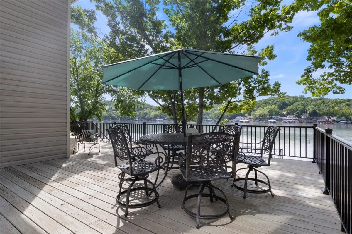 An inviting exterior image of an outdoor dining set with an umbrella, water view, and surrounding trees. The setup encourages al fresco dining, socializing, and enjoying nature at the water’s edge, all under the glow of either morning or evening light.