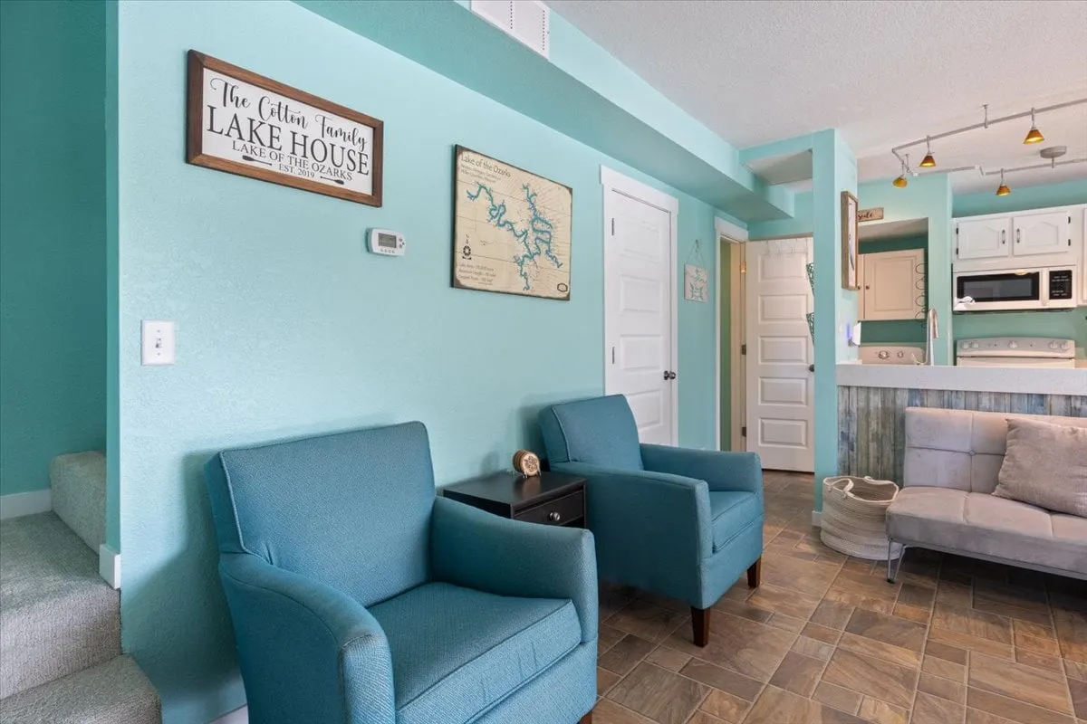 A welcoming living area with turquoise walls, comfortable seating, lake house signage, and a map of the lake. The room is designed for group activities like playing games or enjoying conversations, with an inviting and colorful atmosphere.