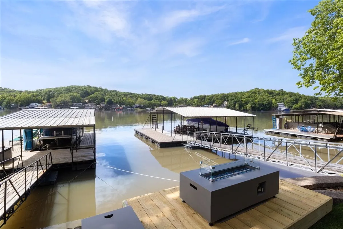 A serene view of the lake featuring docks, lush greenery, and a fire pit by the water. This setting is perfect for evening gatherings or barbecues, and the tranquil atmosphere is ideal for creating family memories.
